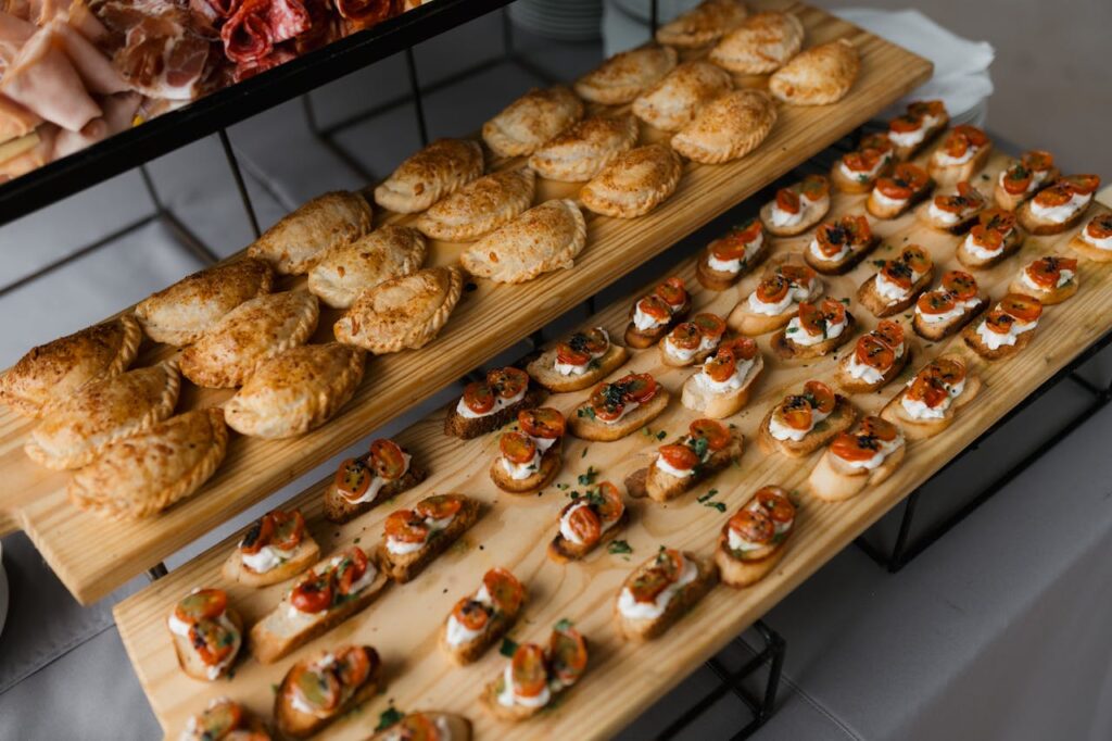 Top-down view of a variety of savory pastries and bruschetta arranged on wooden trays for an event.