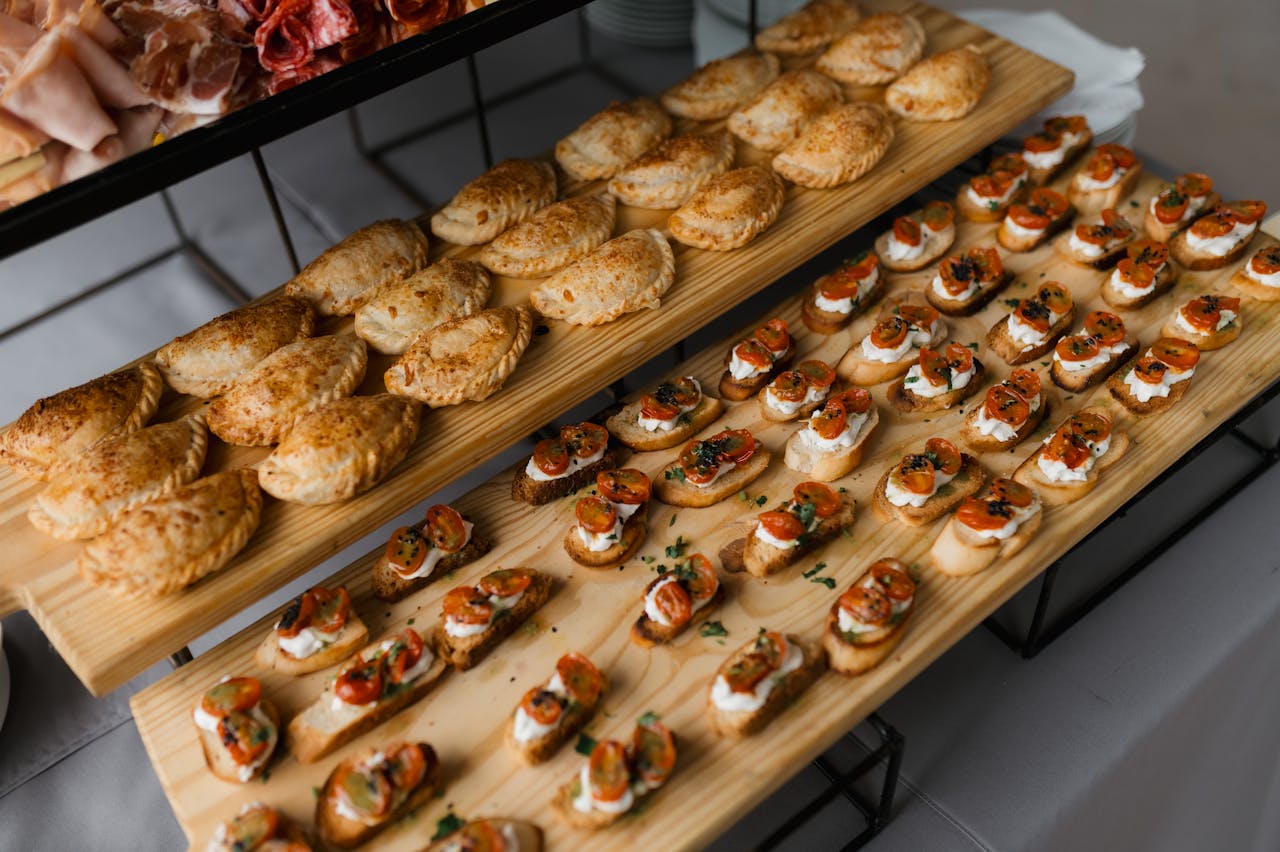Top-down view of a variety of savory pastries and bruschetta arranged on wooden trays for an event.